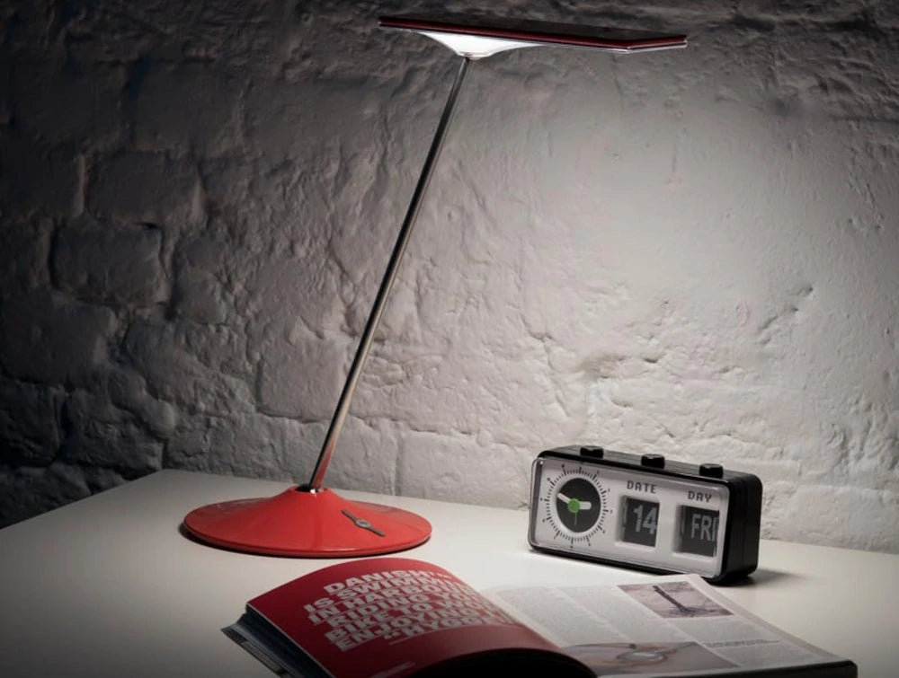 Humanscale Horizon 2 Adjustable Desk Light With Touch Dimming Feature In Red On White Table With Clock And Book