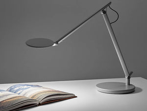 Humanscale Nova Adjustable Desk Light With Charging Desktop Base 5 In Gray On White Table With Book