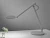 Humanscale Nova Adjustable Desk Light With Charging Desktop Base 6 In Gray On White Table With Plant