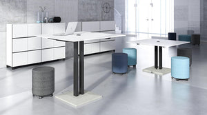 Narbutas Jazz Sit Stand Electric Meeting Table In White Top Finish With Grey Mobile Pouff And White Cupboard In Office Setting