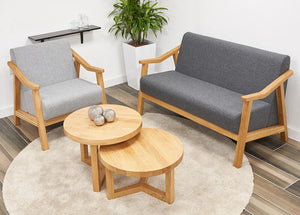 Strut Round Coffee Table In Oak Finish With Grey Armchair And White Plant Pot In Living Room Setting