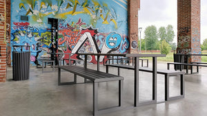 Urbantime .H24 Outdoor Table Integrated Benches In Black Finish With Graffiti Wall In Cafeteria Setting